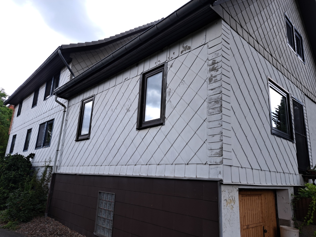 Die unsanierte Fassade des Hauses mit vorgehängten Faserzementplatten und zweifach verglasten Fenstern